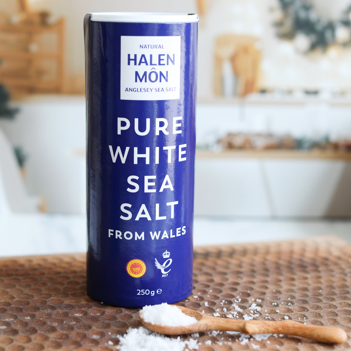 Halen Mon pure white sea salt container on a wooden surface with a blurred kitchen background