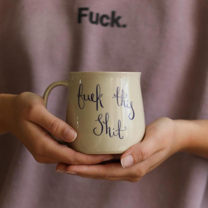 A handmade mug with the text ‘fuck this shit’ in cursive writing from Glosters pottery.
