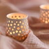 A handmade ceramic candle holder with a lit candle inside. Made by Glosters.
