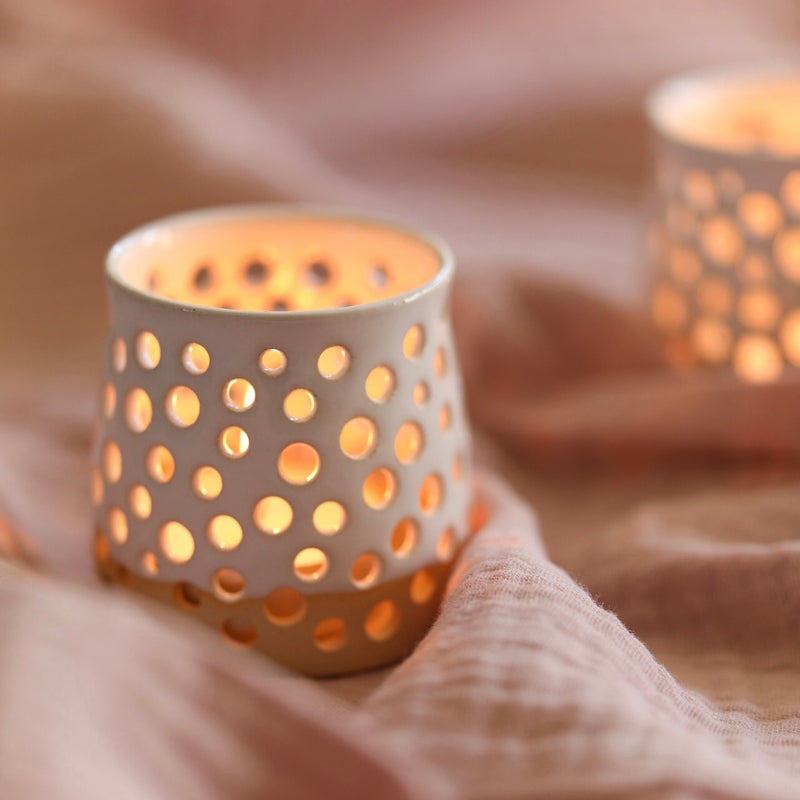 A handmade ceramic candle holder with a lit candle inside. Made by Glosters.