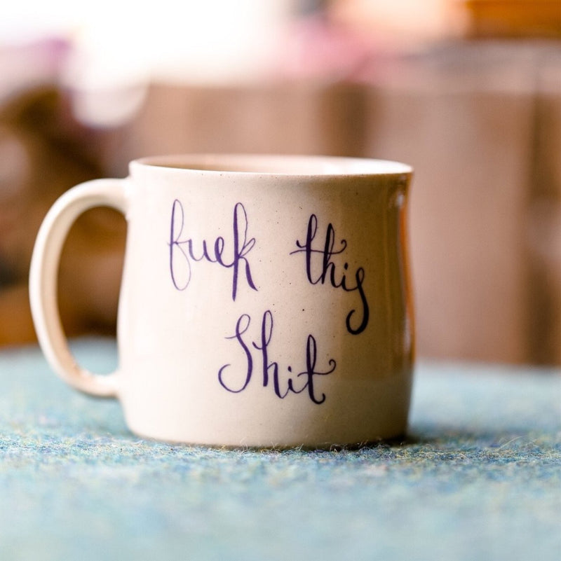 A handmade mug with the text ‘fuck this shit’ in cursive writing from Glosters pottery.